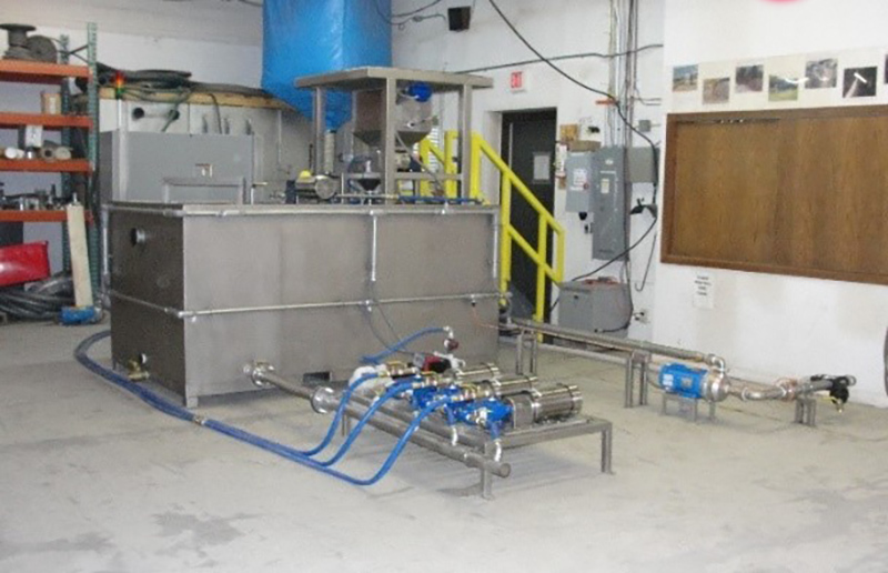 Système de dilution de polymères en acier inoxydable Clearwater Industries, modèle 500, photographié de côté pour montrer son système de pompe, sa trémie de polymères et son système d’alimentation en polymères secs.