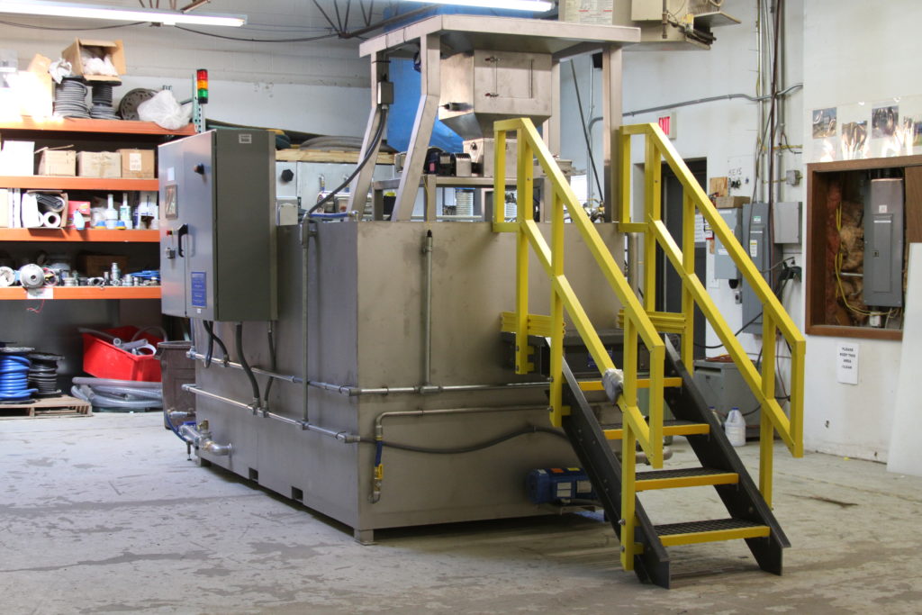 Clearwater Industries Model 800 Stainless Steel Big Bag polymer make-down system pictured in the manufacturing department and displaying the big bag pan that holds it above the hopper, it's control panel and operator staircase.