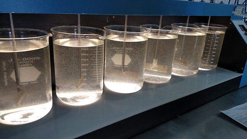 Industrial Water Testing Six glass lab beakers with clear liquid in them setup in a water jar testing system.