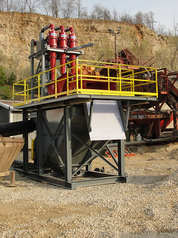 A stationary fines recovery system with three red cyclones, yellow railing and a grey tank.
