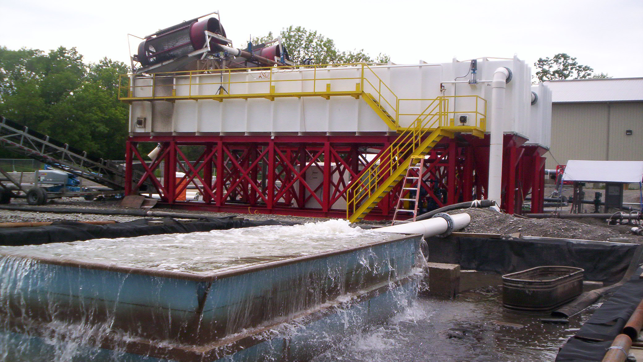 Large rectangular clarifiers in the background with rotary trommel screens on top of them and a clean water overflow basin in the foreground.
