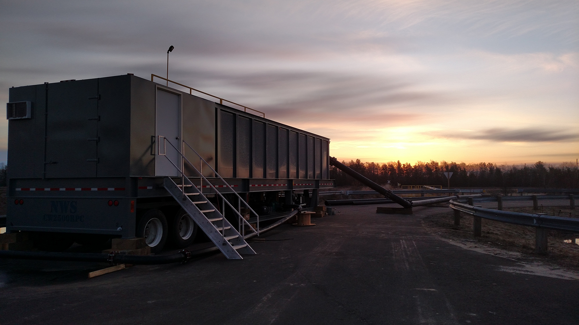 A portable water clarifier with stairs going up to a white door on the back of the clarifier and a sunset in the background.