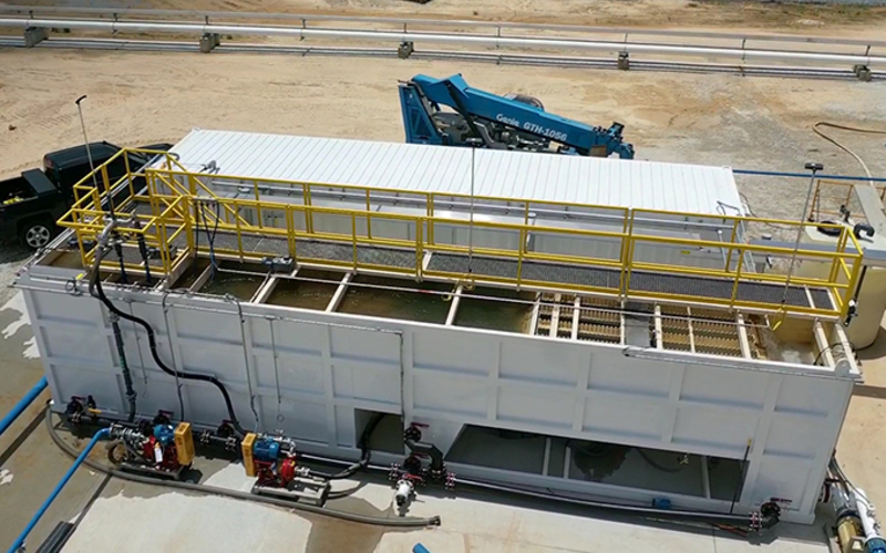 Una imagen que mira hacia abajo en ángulo a un gran clarificador de agua estacionario blanco con un camión y otro equipo industrial en un lugar de trabajo.