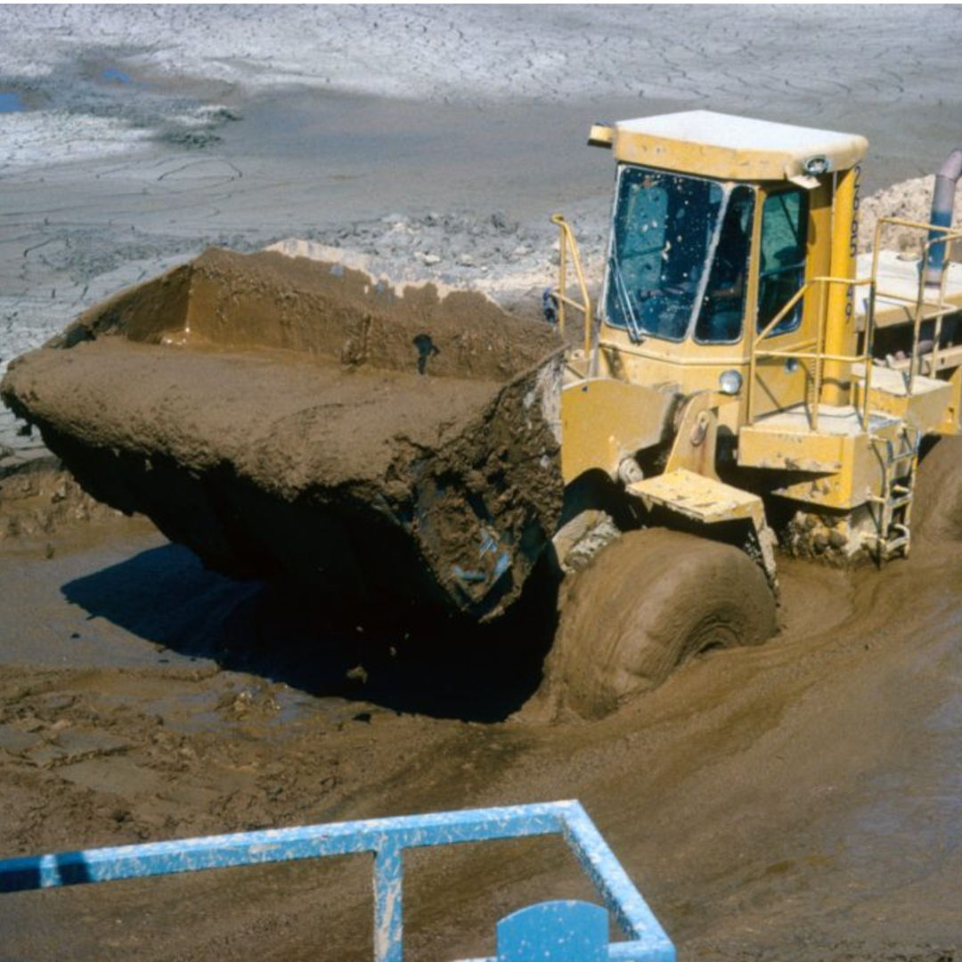 A front loader driving through a muddy pond with a bucket of soupy mud.