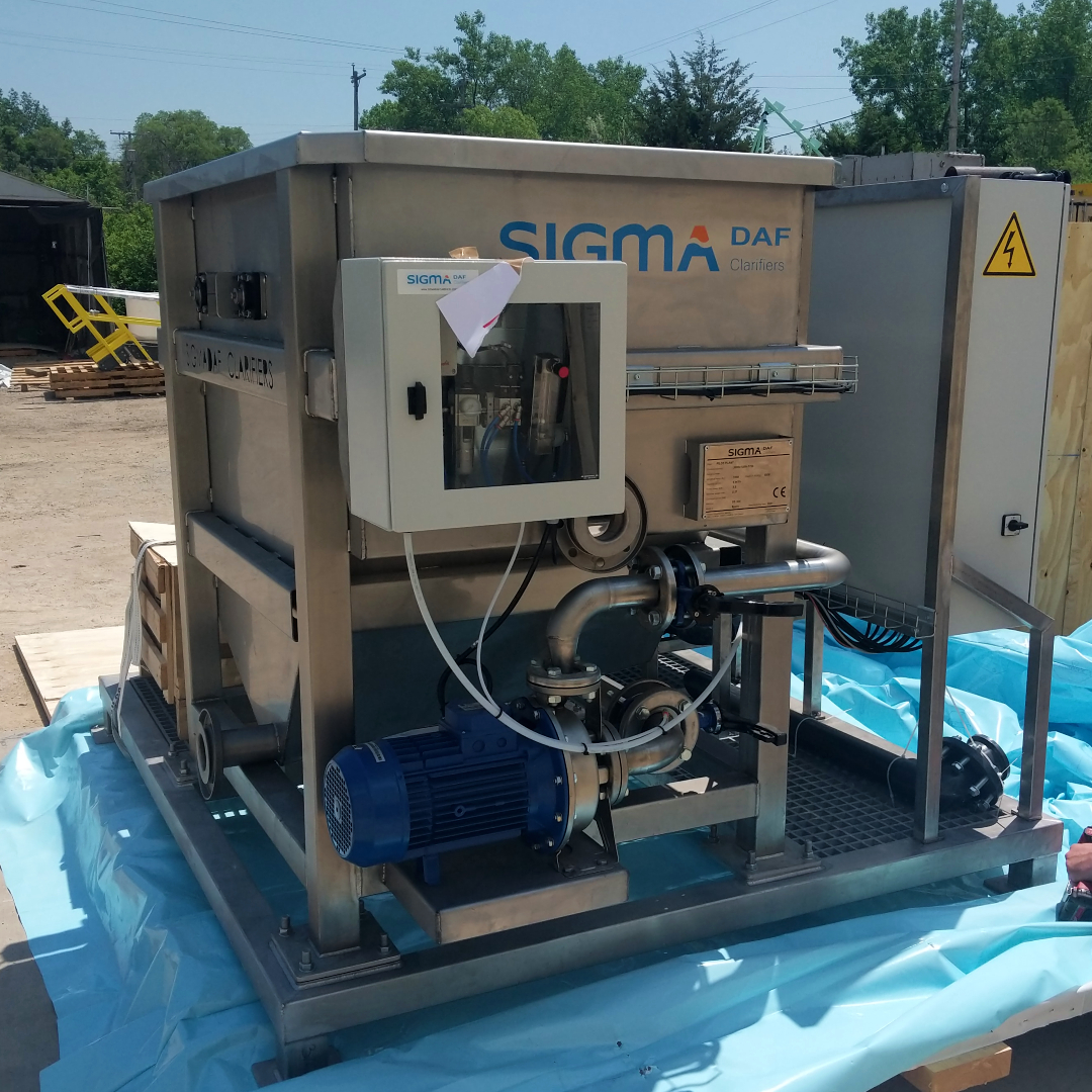 A DAF skid pictured outside with the stainless steel DAF tank pictured in the foreground and unidentifiable components in the background.