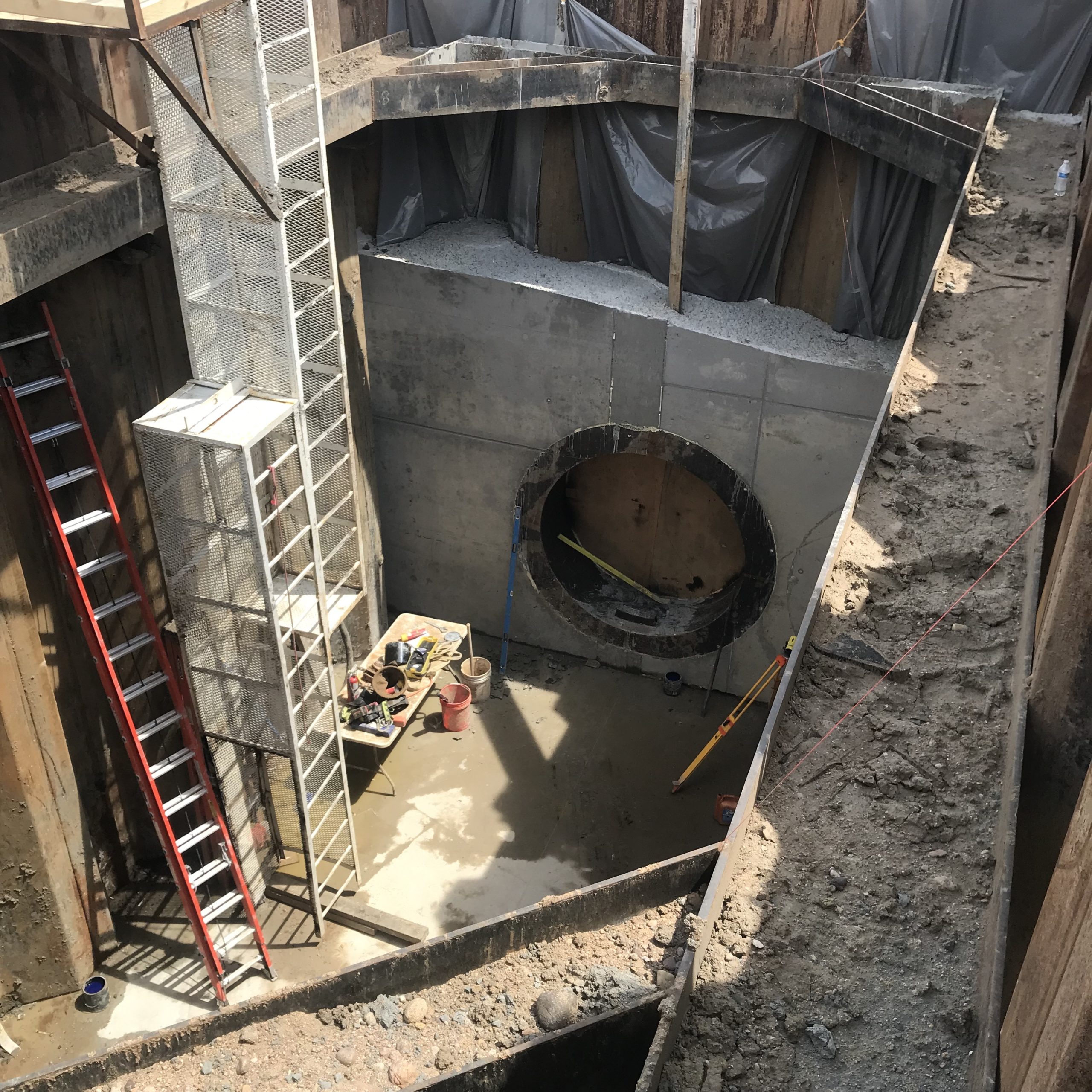 A large pit in the ground with ladders, buckets and other equipment where a drilling and tunneling machine will begin its work.