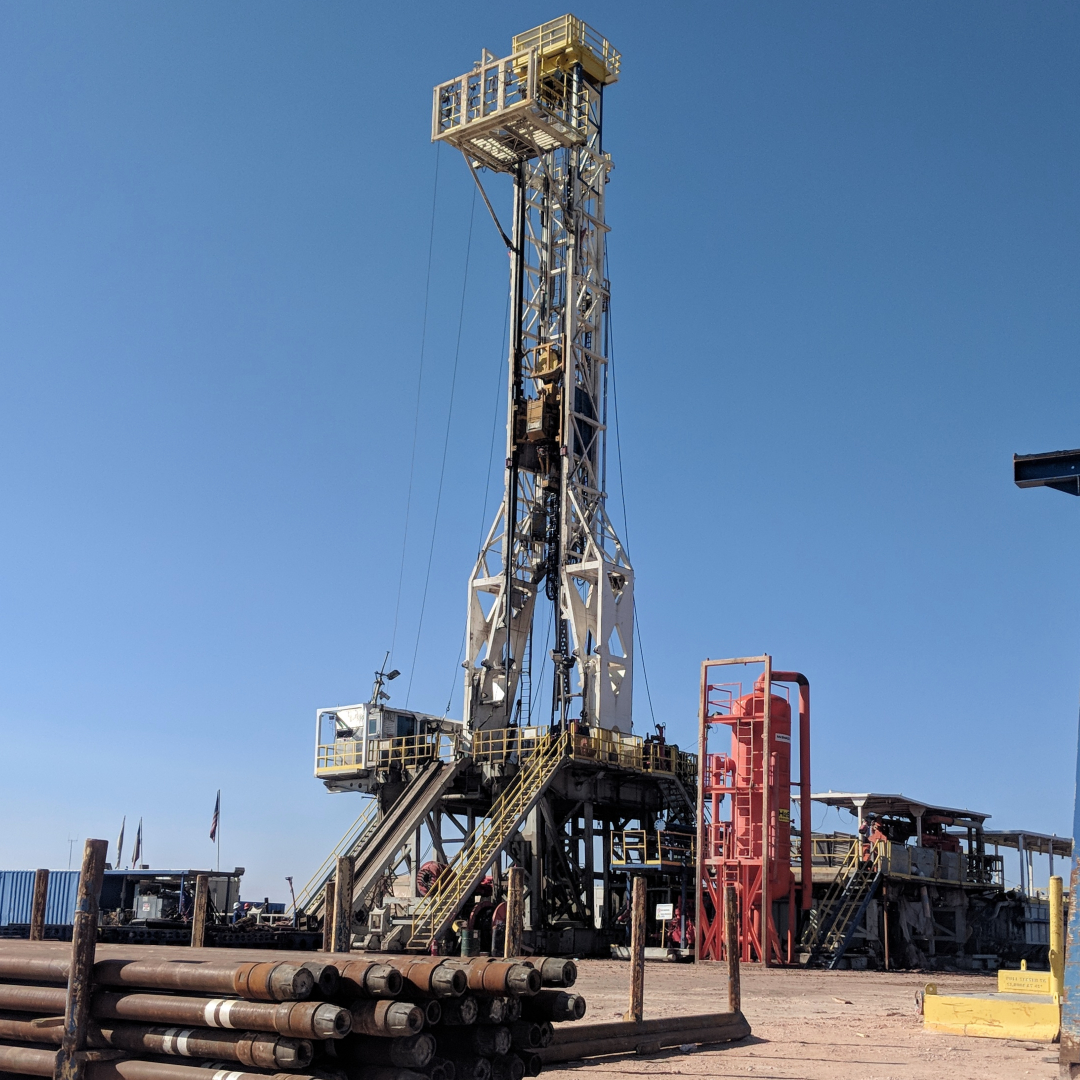 A drilling rig setup on land with drilling pipes in the foreground.