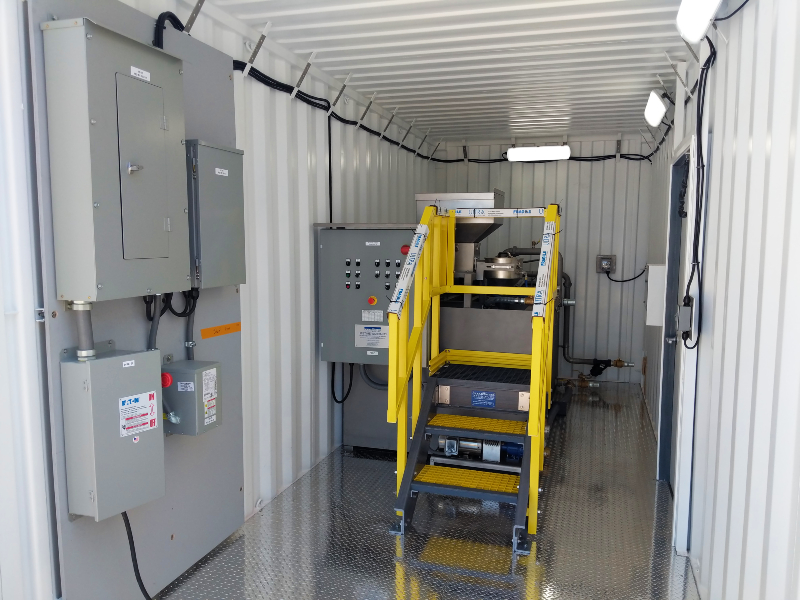 A dry polymer system in a ten foot container with a control panel an electrical panel on the wall.