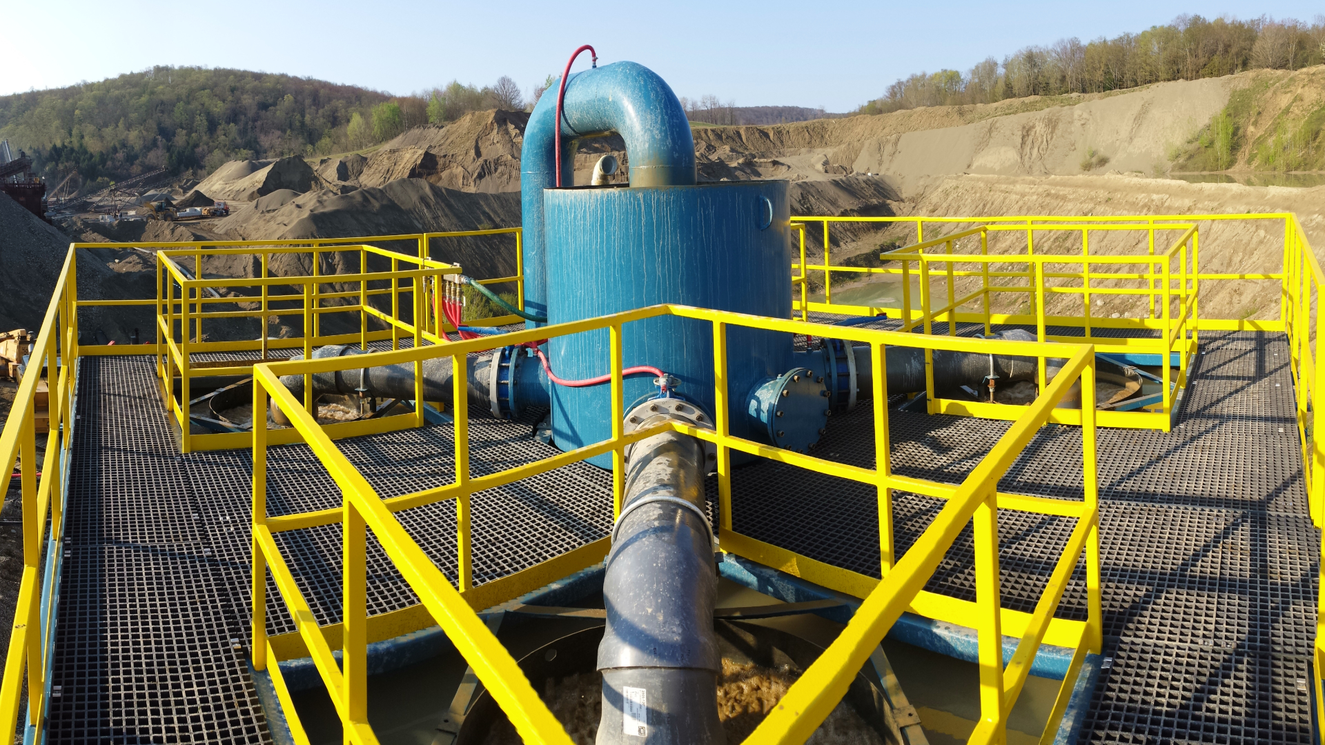 A bridge deck with large blue pipes on top of an industrial clarifier.
