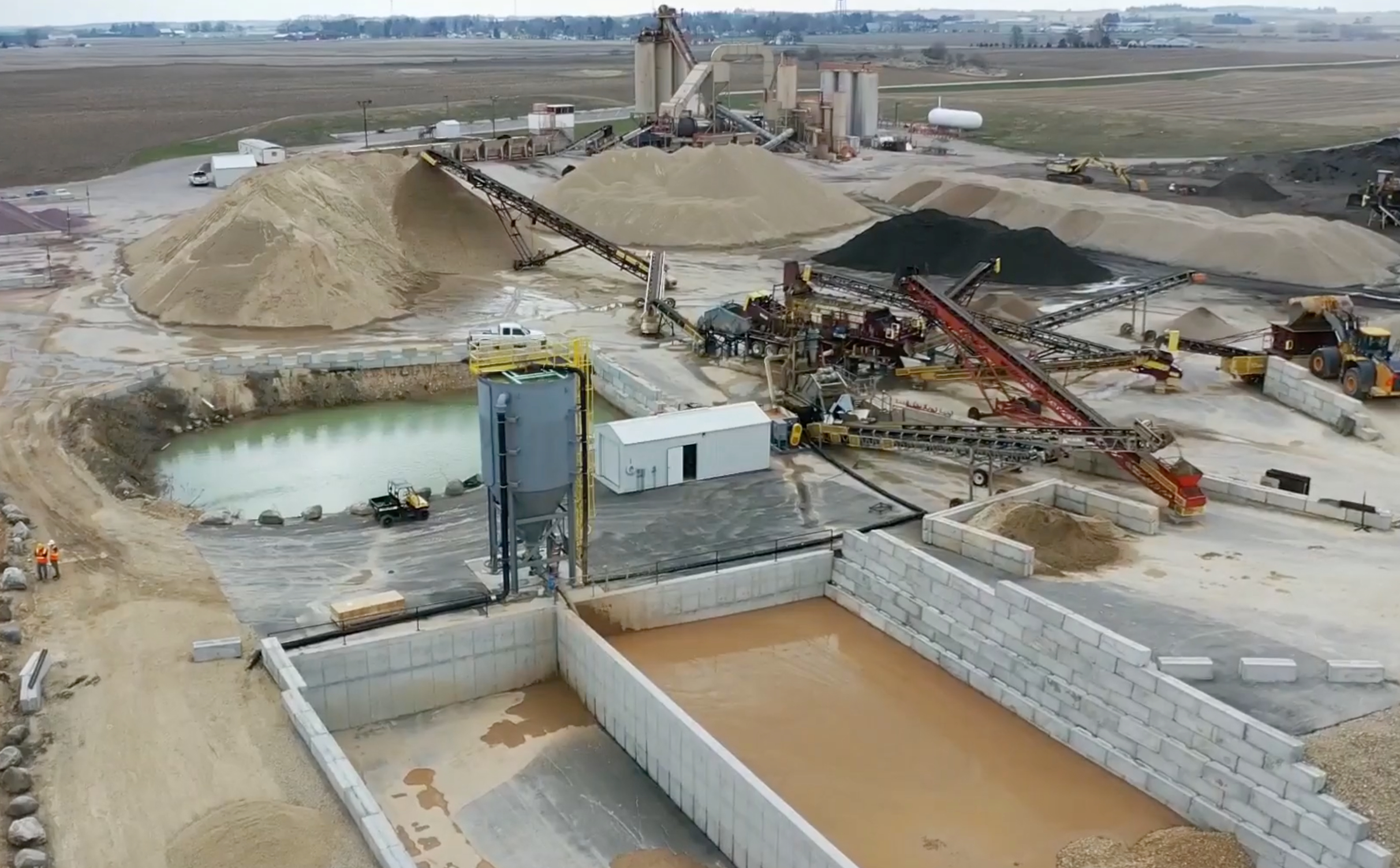 An arial photo of an aggregate production site with mud cells and clarifier in the foreground and aggregate piles and equipment in the background.