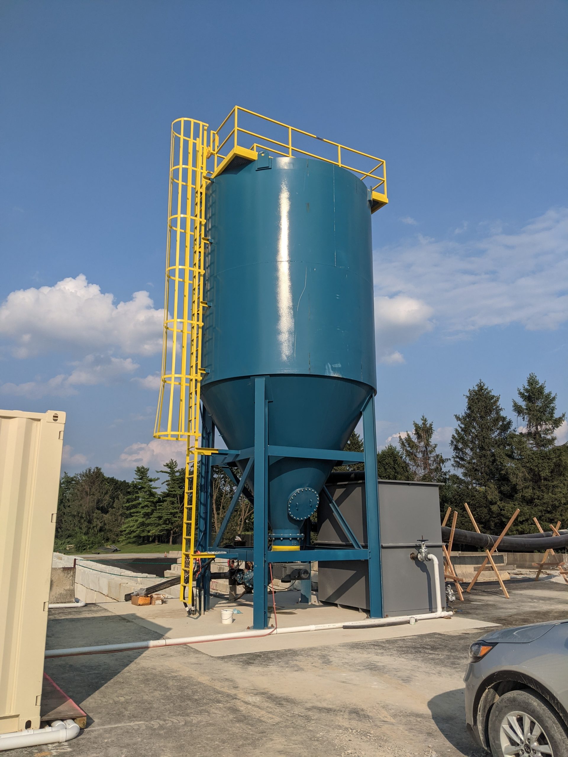 A large, vertical, blue and metal clarifier with a yellow ladder in the sun.