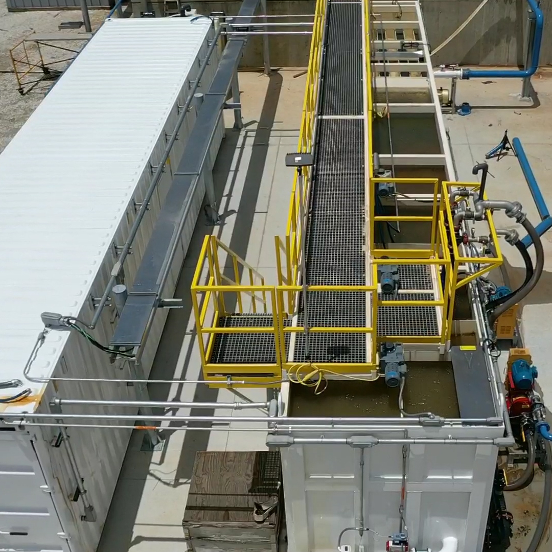 A white metal shipping container and white tank with water in it next to each other.