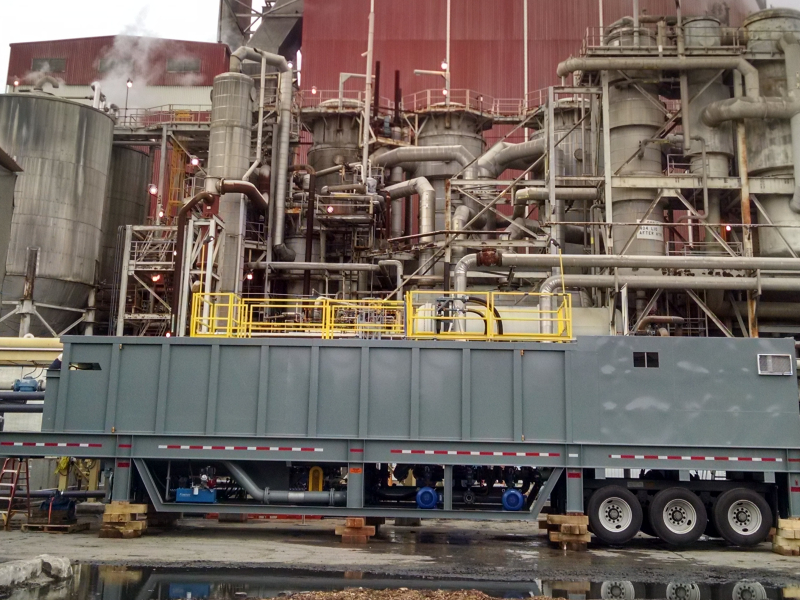 A large grey portable water clarifier cribbed up outside of a paper mill.