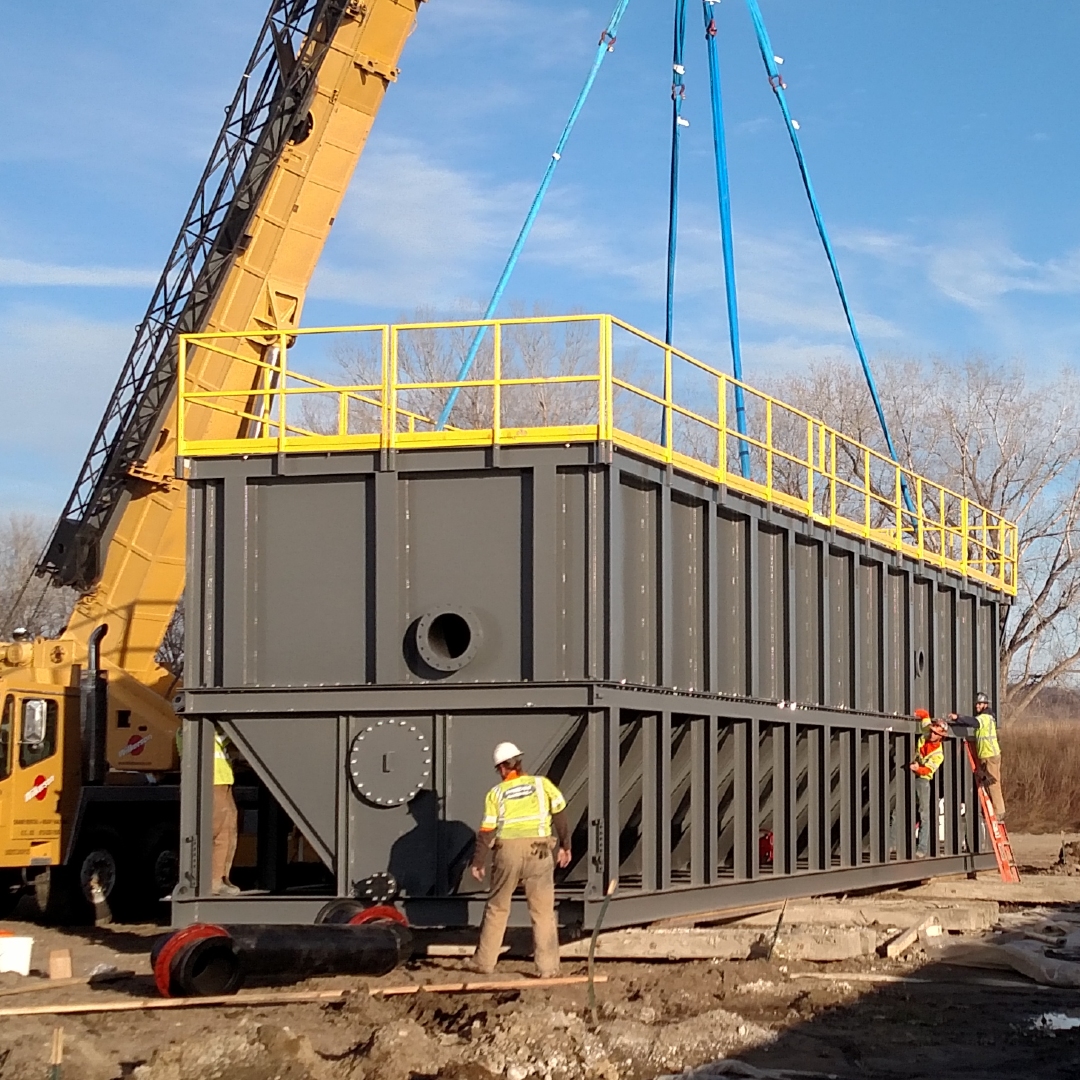 A large grey tank clarifier being placed by a crane and workers.