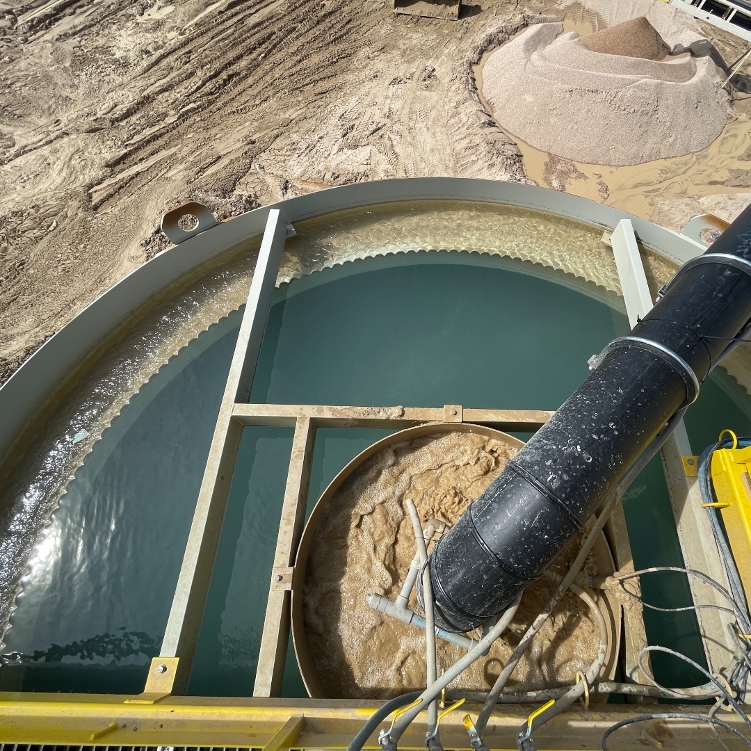 A black pipe feeding brown process water into a clarifiers center-well and clean water overflowing weirs from the peripheral well.