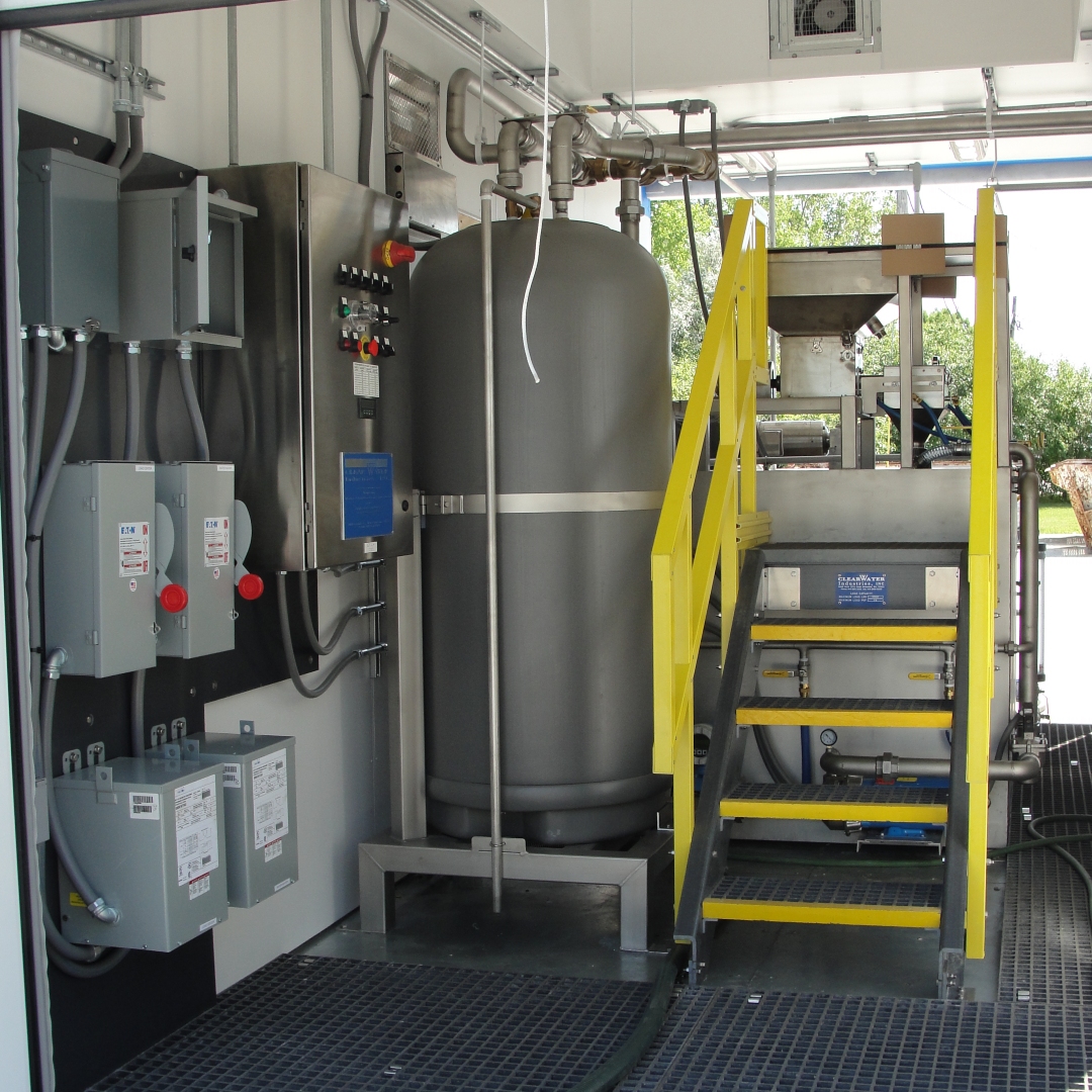 A grey tank, power distribution board, and chemical preparation system inside a shipping container with all the doors open.