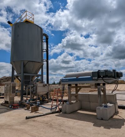 A large grey clarifier and centrifuge next to each other with plumbing, tanks, and other equipment in between.