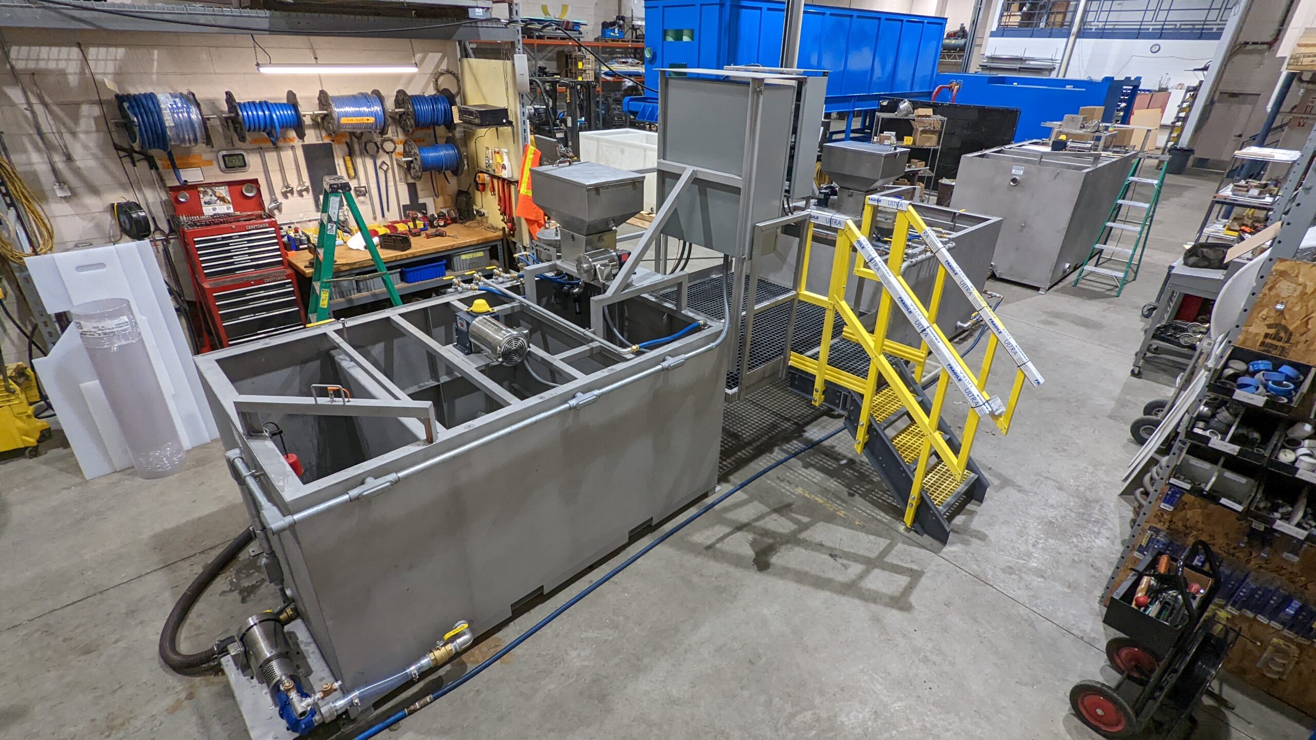M500SS 1 Several rectangular stainless steel tanks with motors and piping inside a manufacturing facility.